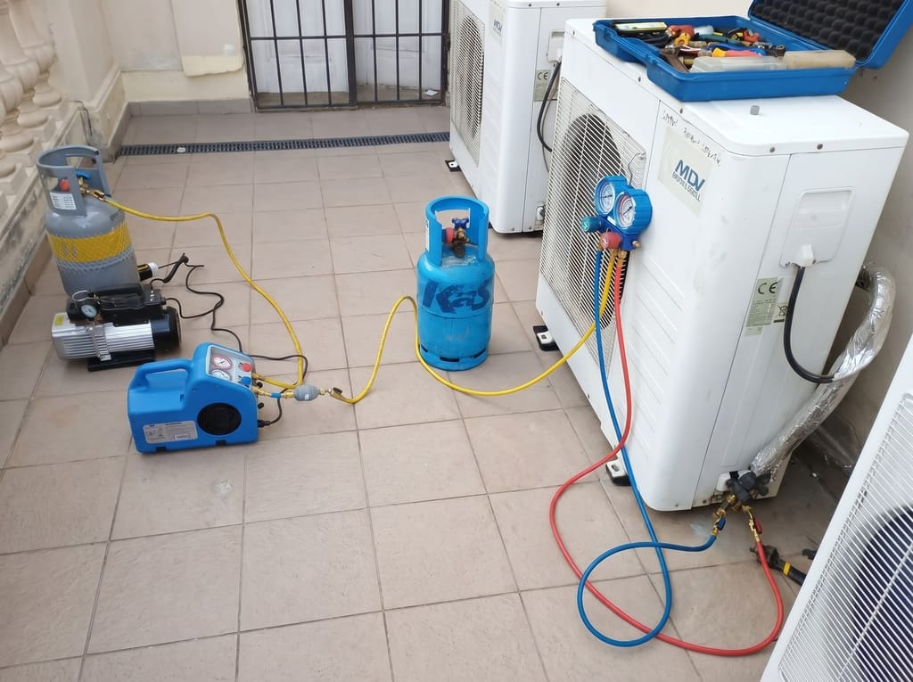 Servisní zázemí Luftmaru u dvojice venkovních klimatizačních jednotek — vakuová pumpa, manifold s manometry napojený do servisních portů a láhev chladiva při pravidelném servisu